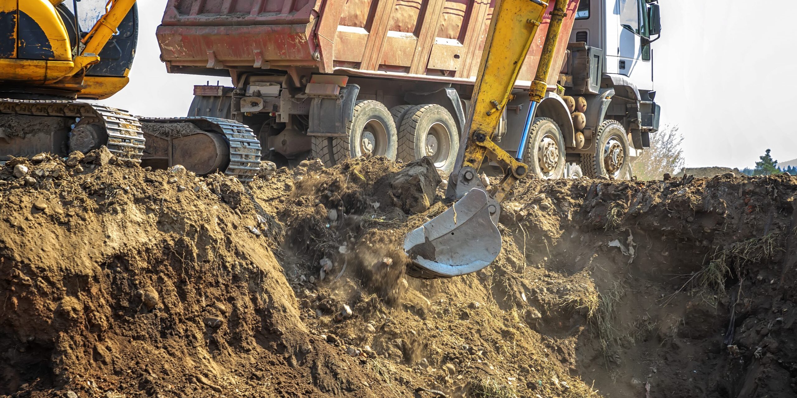 Excavator is loading excavation on the truck. Heavy construction equipment consisting of a boom, dipper or stick, bucket, and cab on a rotating platform.